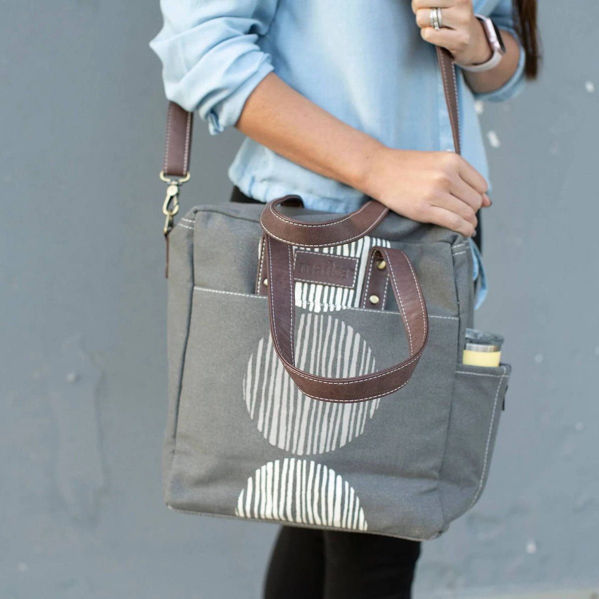 Gray tote bag with brown handle held by a person against a gray background