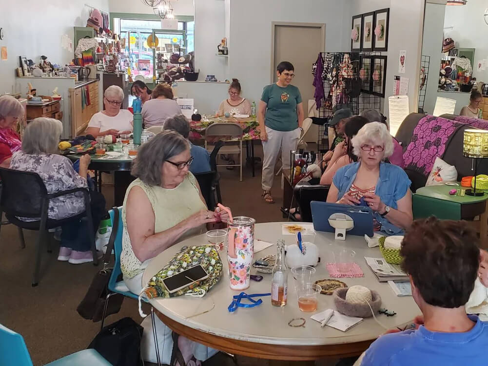 Group of people gathered around tables at a yarn shop