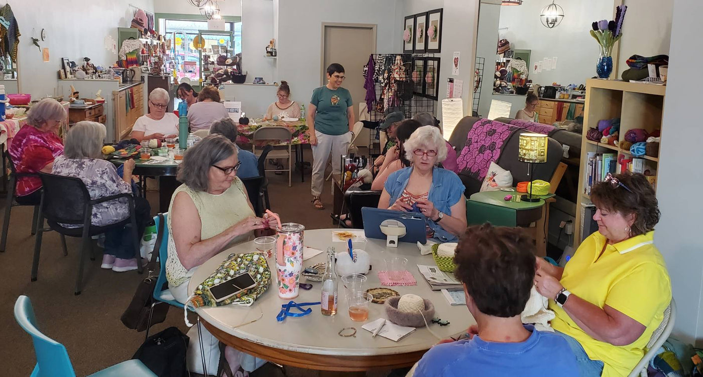 Knitters and crocheters sitting at tables in a yarn store
