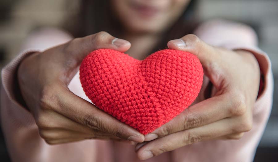 Red heart-shaped object held in hands against a blurred background