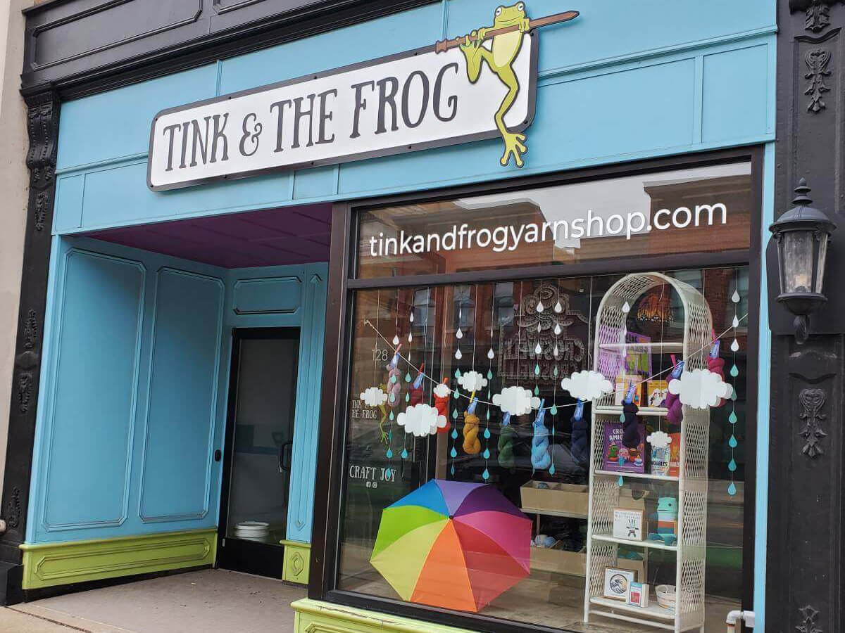 Storefront of Tink & The Frog yarn shop with colorful display and sign.