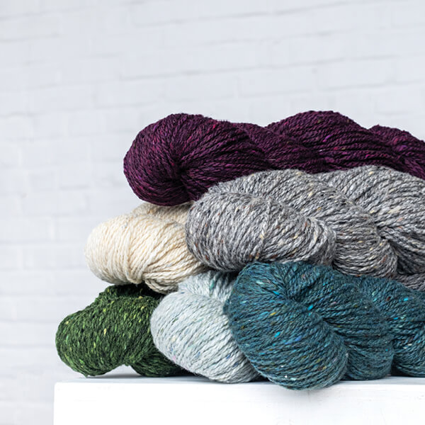 A pile of several hanks of Lucky Tweed yarn in a variety of colors
